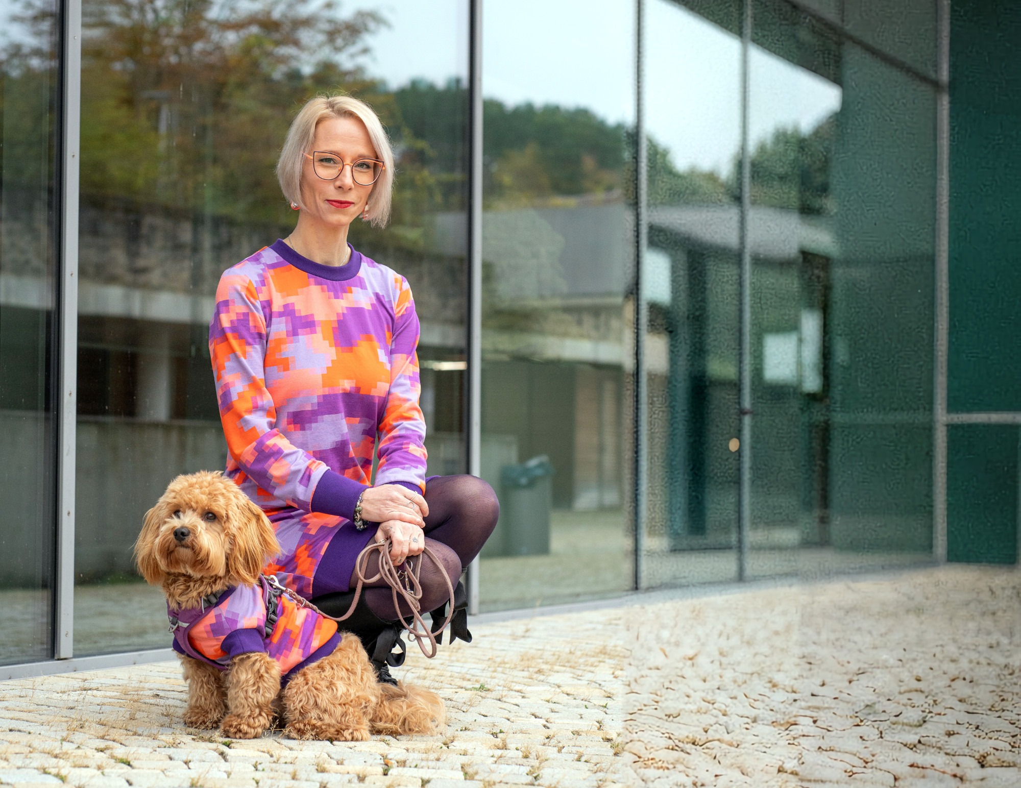 Ganzkörperportrait von Julia M. Falkenhain kniend neben ihrem Hund Cosmo, der sie bei Beratung und Coaching unterstützt.