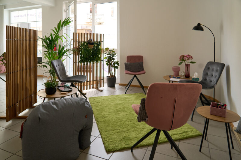 Ein Blick in die Beratungsecke mit Sichtschutz, mehreren gepolsterten Stühlen mit Kissen, einem weichen Teppich und einem Sitzsack in der Form eines Elefanten.