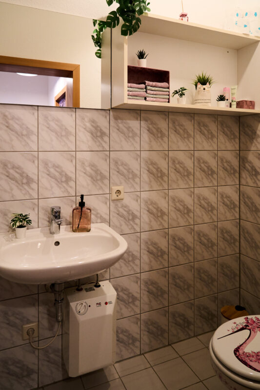 Ein Blick in das Gäste-Bad mit Waschbecken, WC und einem Regal mit Handtüchern und einigen hilfreichen Artikeln.