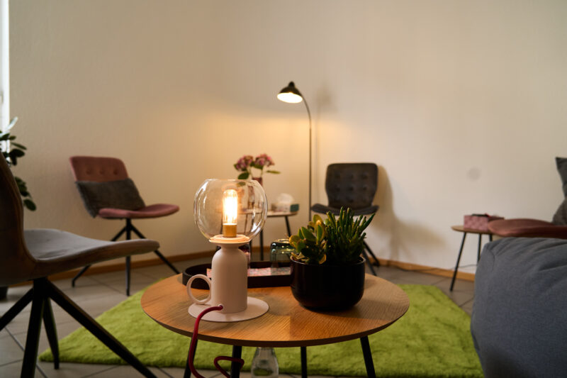 Ein Ausschnitt der Beratungsecke mit Stehlampe, gepolsterten Sitzgelegenheiten, kleinen Tischen und warmen Lichtern.