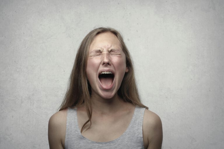 Das Portrait einer jungen Frau, die mit zusammengekniffenen Augen laut schreit.